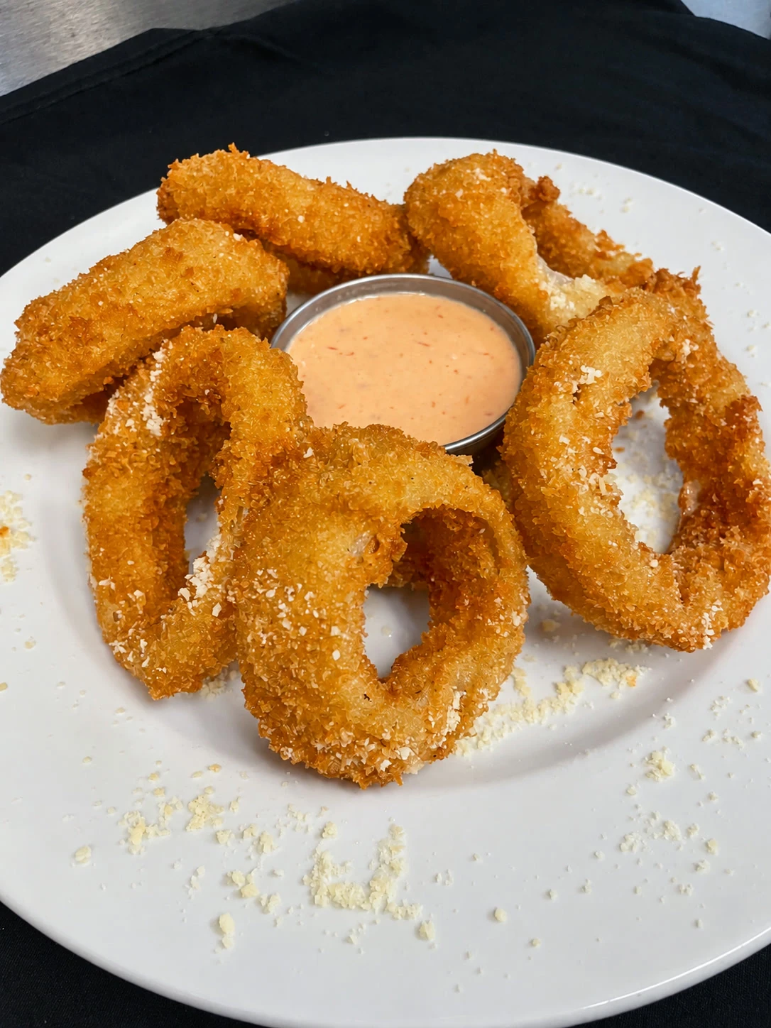 Panko-crusted onion rings arranged around a cup of dipping sauce